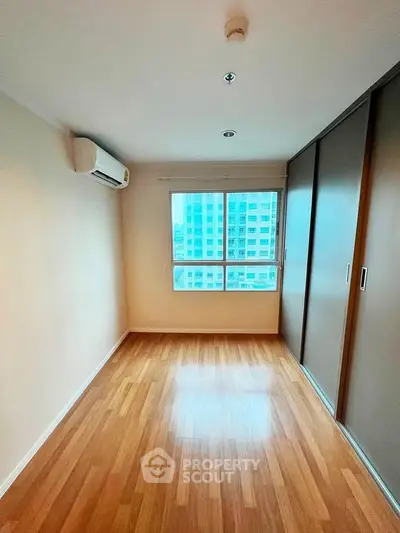 Spacious bedroom with wooden flooring and large window in modern apartment.