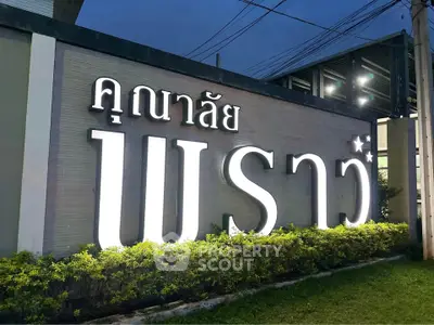 Illuminated real estate sign with lush greenery at dusk, showcasing modern property entrance.