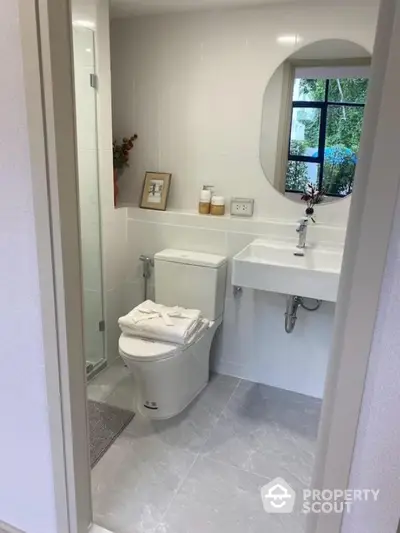 Modern bathroom with sleek design and round mirror, featuring a compact layout and stylish fixtures.