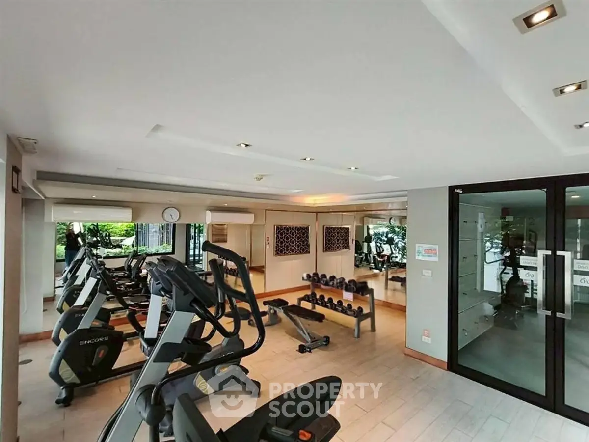 Spacious gym with modern equipment and mirrored walls in luxury apartment building.