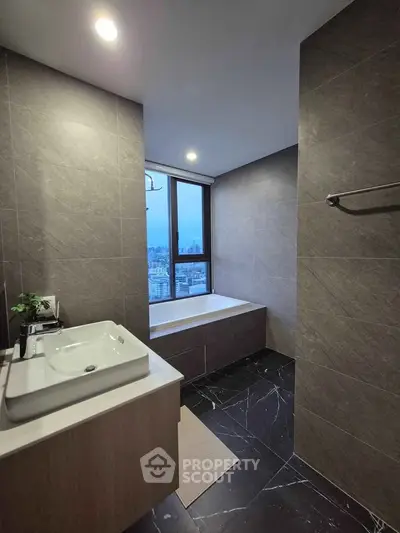 Luxurious bathroom with city view, featuring modern sink and bathtub, elegant dark tiles, and ambient lighting.