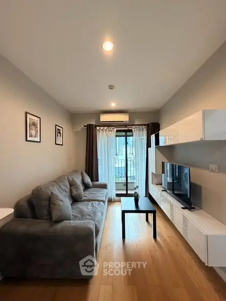 Modern living room with cozy sofa and entertainment unit, featuring large window and wooden flooring.