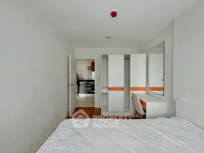 Modern bedroom with white furniture and a glimpse of a sleek kitchen in the background.