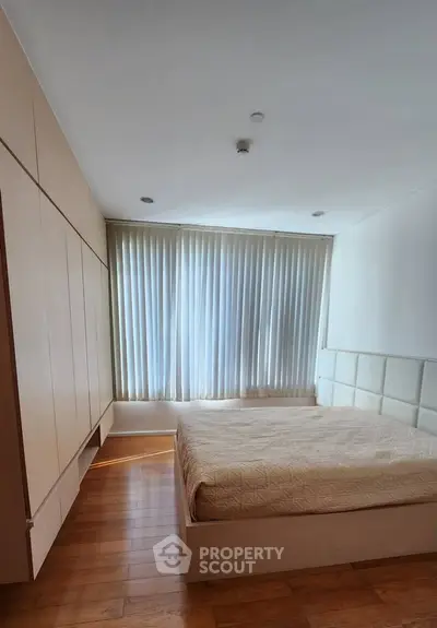 Spacious bedroom with elegant wooden flooring and large window draped with curtains.