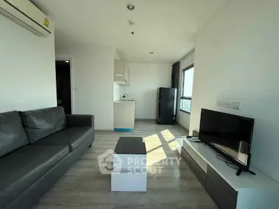 Modern living room with sleek furniture and natural light, featuring a compact kitchen and city view.