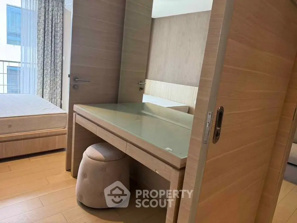 Modern bedroom with stylish wooden furniture and glass-top desk, featuring a cozy ambiance and natural light.