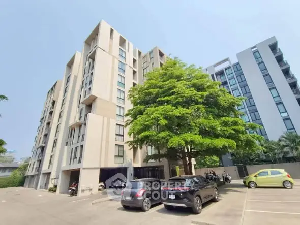Modern apartment building with parking area and lush greenery, ideal urban living.