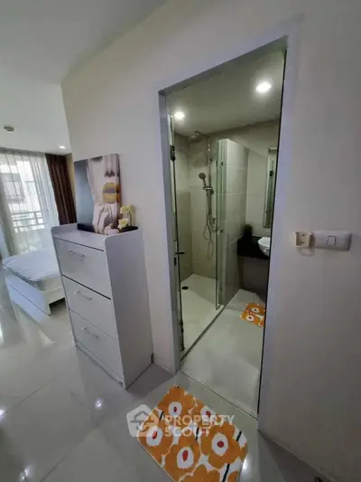 Modern apartment interior with bedroom and compact bathroom featuring glass shower enclosure.