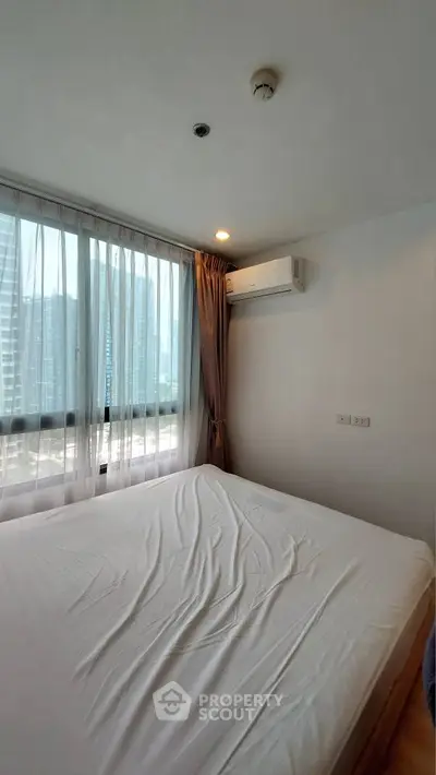 Modern bedroom with large window and city view, featuring air conditioning and natural light.