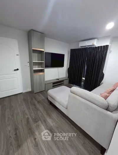 Modern living room with sleek furniture and dark curtains, featuring a wall-mounted TV and air conditioning.