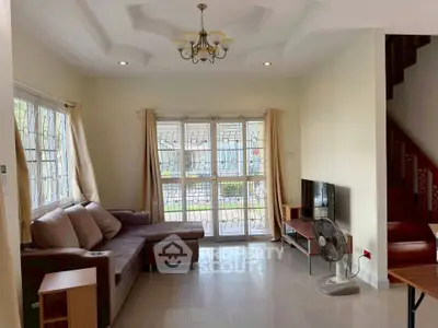Spacious living room with elegant chandelier and large windows offering natural light.
