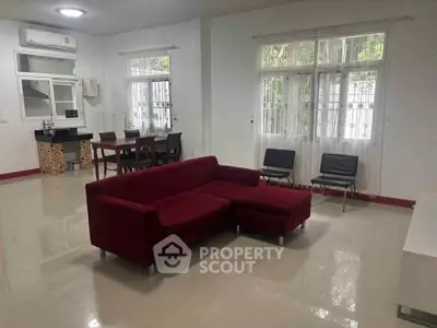 Spacious living room with modern red sofa and dining area, featuring large windows for natural light.