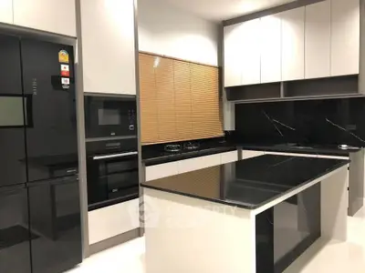 Modern kitchen with sleek black countertops and built-in appliances, featuring a central island and stylish cabinetry.