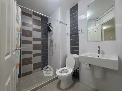 Modern bathroom with sleek design, featuring a shower, toilet, and sink in a stylish tiled setting.