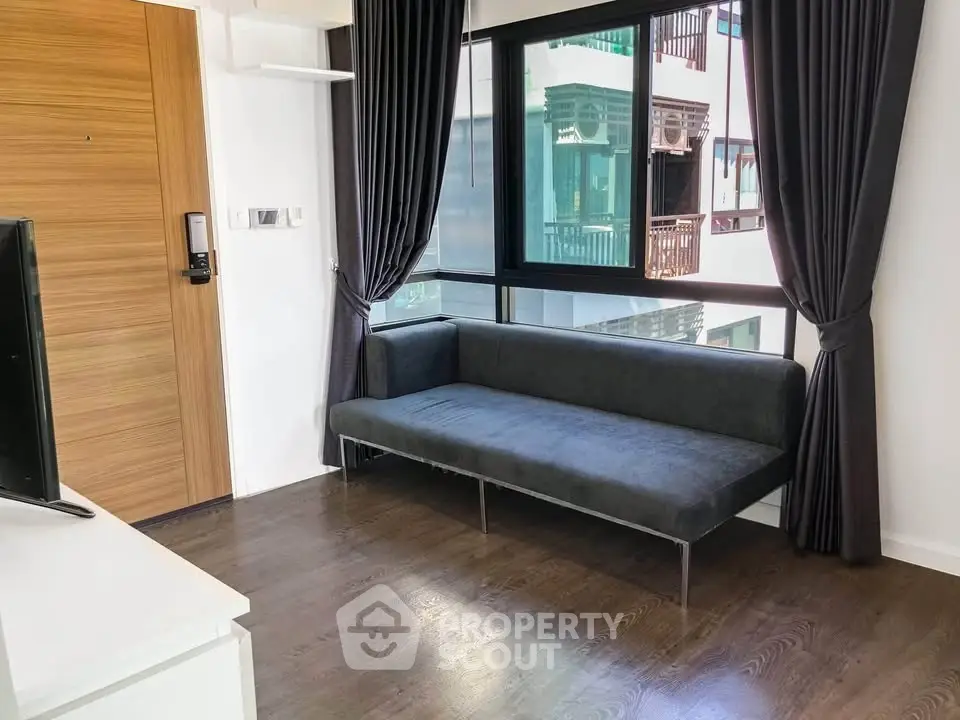 Modern living room with sleek sofa and large window, featuring elegant dark curtains and wooden flooring.