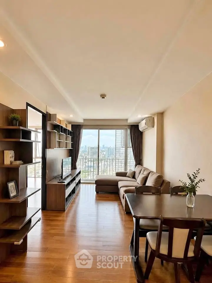 Spacious living room with city view, wooden flooring, and modern furniture in a high-rise apartment.
