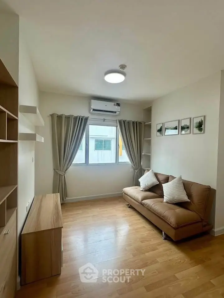 Cozy living room with wooden flooring and modern sofa, featuring natural light from large window.