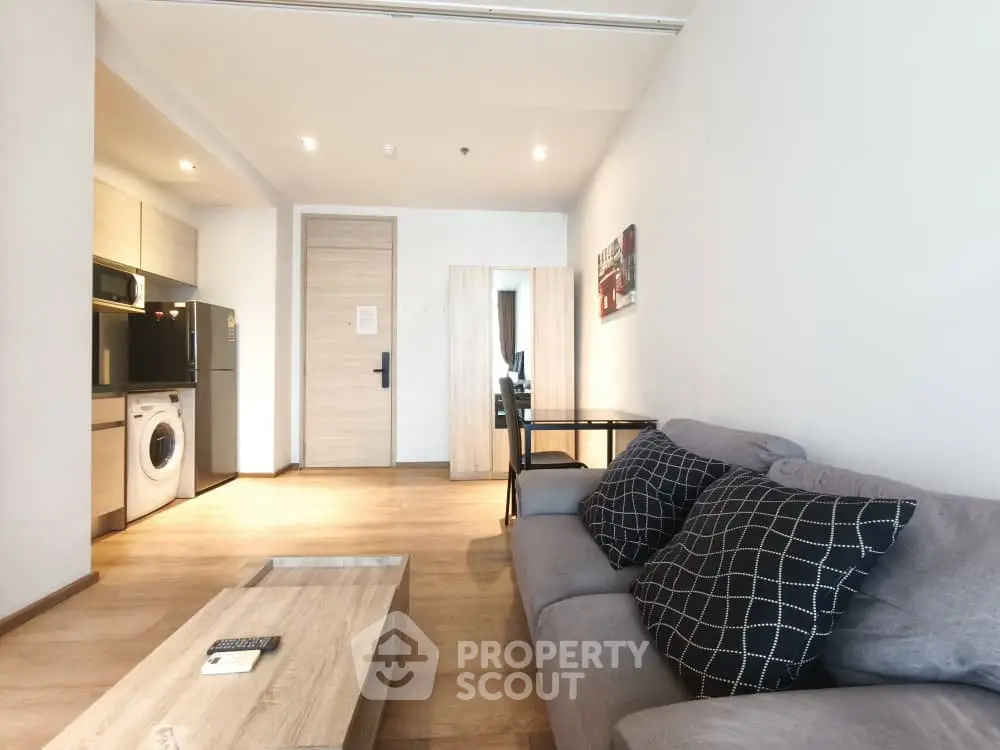 Modern living room with open kitchen, featuring sleek furniture and wooden flooring.