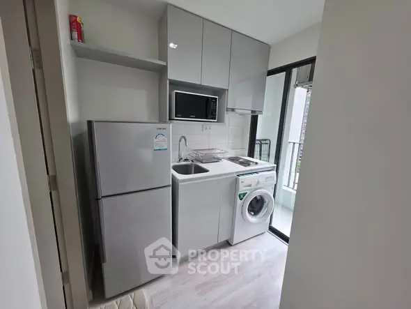 Modern compact kitchen with appliances including fridge, microwave, and washing machine.