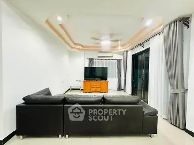 Spacious modern living room with sleek black leather sofa and large TV, perfect for relaxation.