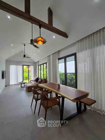 Spacious modern living room with high ceilings, elegant furniture, and large windows offering lush garden views.