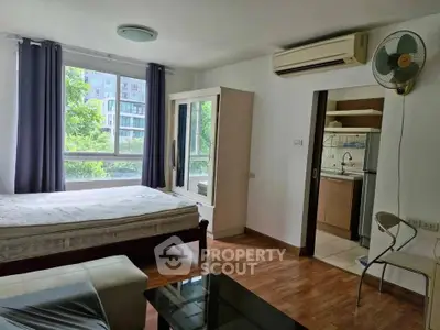 Modern studio apartment with wooden flooring, large window, and compact kitchen area.