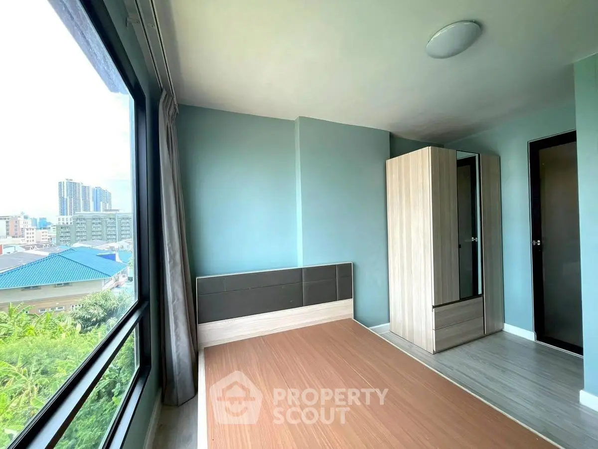 Modern bedroom with large window and city view, featuring sleek wardrobe and minimalist design.