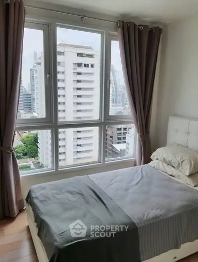Cozy bedroom with large window offering stunning city view in modern apartment.