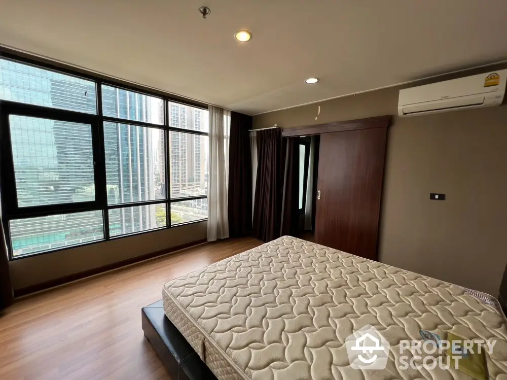 Spacious bedroom with large windows offering stunning city views in modern apartment.