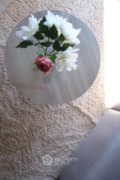 Elegant round glass table with floral centerpiece on plush carpet in cozy living room corner.