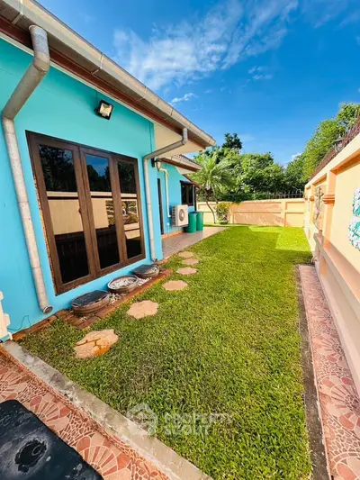 Charming house exterior with lush green lawn and vibrant blue walls, perfect for outdoor relaxation.