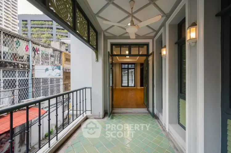 Charming balcony with green tiles and ceiling fan, overlooking urban view, perfect for relaxation.