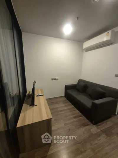 Modern living room with sleek sofa and TV, featuring wooden flooring and air conditioning.