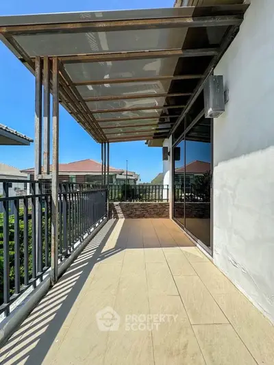 Spacious balcony with modern railing and partial roof, offering a serene view of surrounding rooftops.