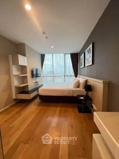Modern bedroom with large window and wooden flooring in a stylish apartment.
