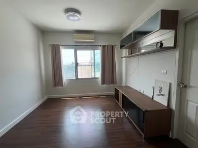 Spacious empty room with wooden flooring and large window, ideal for customization.