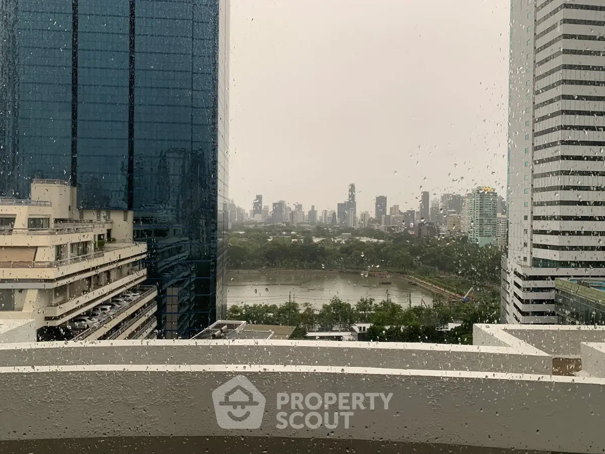 Stunning cityscape view from high-rise building on a rainy day, showcasing urban skyline and lush greenery.