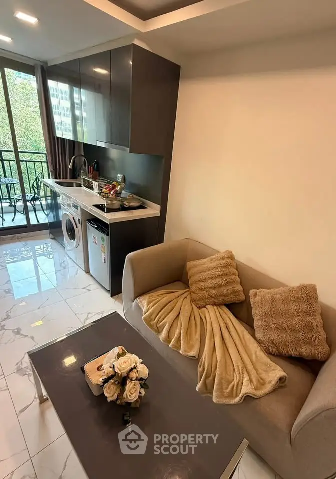 Modern apartment living room with open kitchen and balcony view, featuring cozy sofa and sleek appliances.