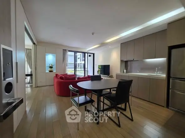 Modern open-plan living room with sleek kitchen and stylish red sofa, featuring wooden flooring and ample natural light.