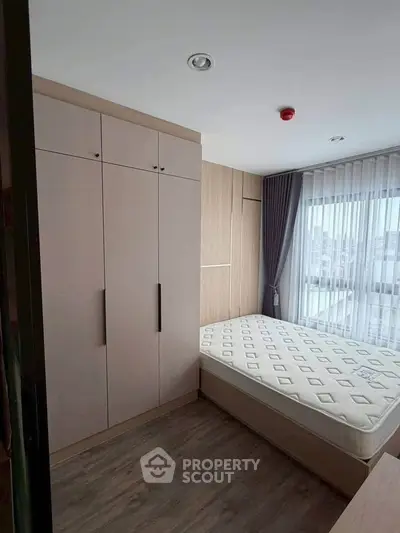 Modern bedroom with large window and built-in wardrobe, featuring a comfortable mattress and elegant curtains.