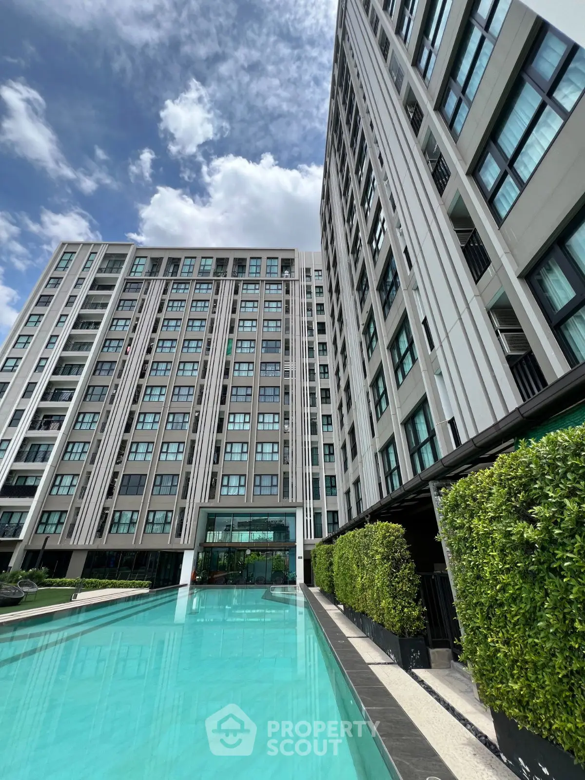 Luxurious modern apartment building with stunning pool and lush greenery under a clear blue sky.