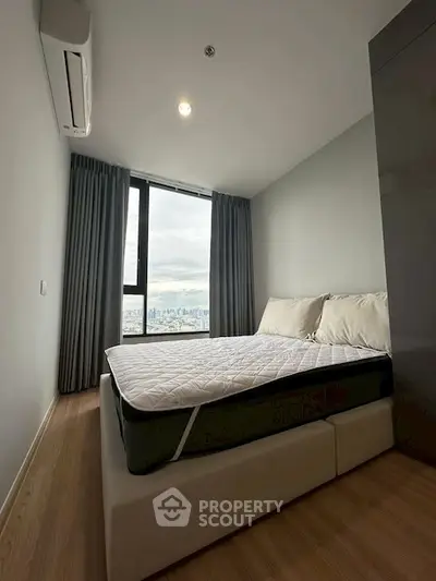 Modern bedroom with city view, featuring a cozy bed and large window.