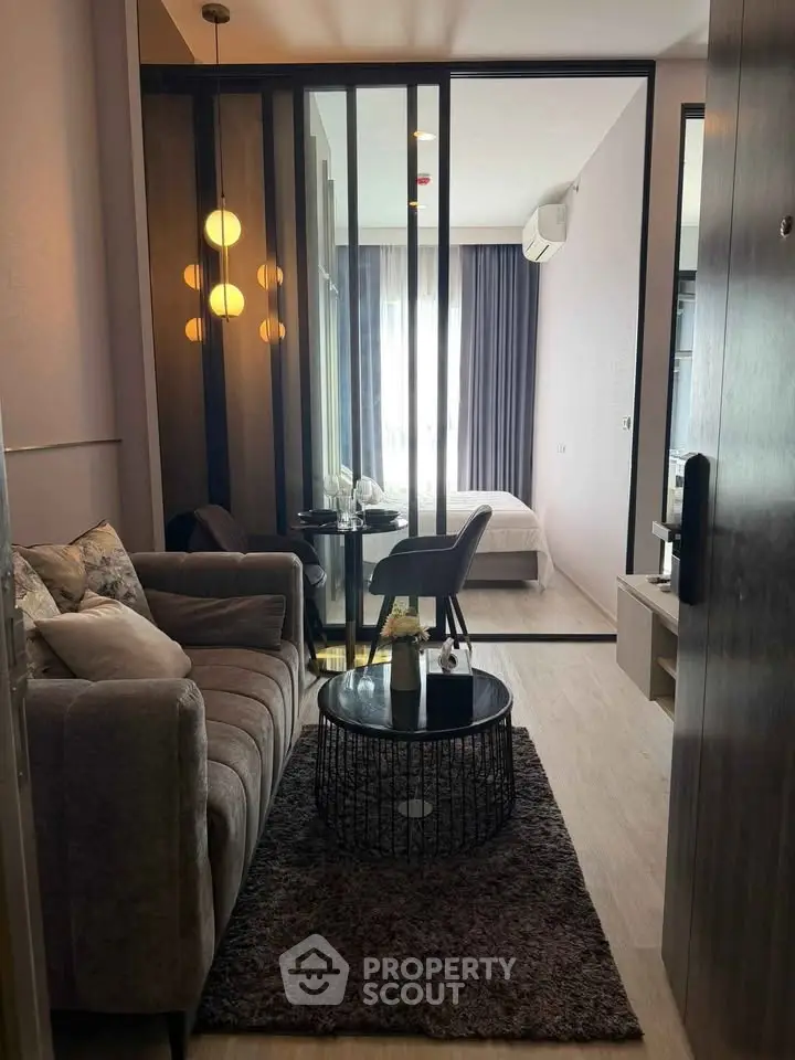 Modern apartment interior with cozy living room and stylish bedroom separated by glass partition.