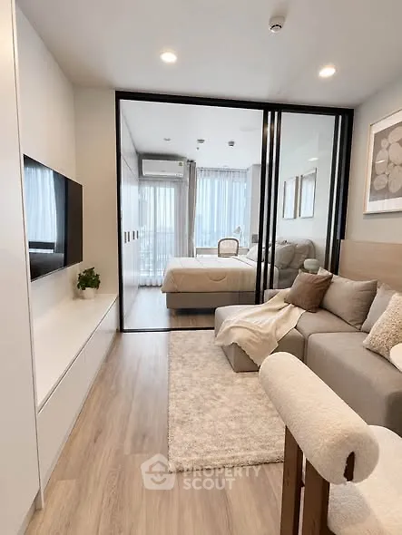 Modern living room with cozy sofa and view into stylish bedroom through glass doors.