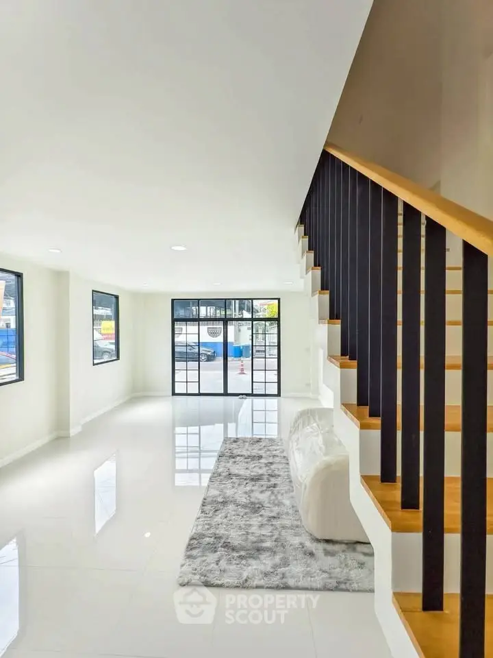 Spacious modern living room with sleek staircase and large windows for natural light.