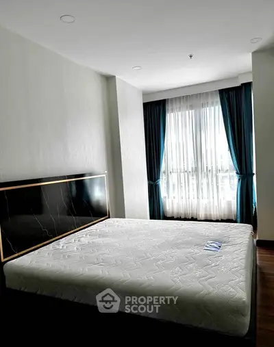 Spacious bedroom with large window and elegant curtains in modern apartment.