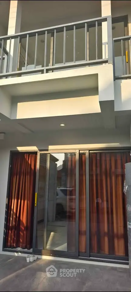 Modern two-story building exterior with large glass doors and balcony, showcasing contemporary architectural design.