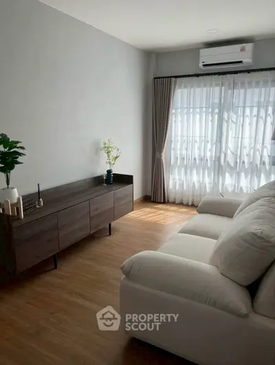 Modern living room with natural light, featuring a sleek sofa and stylish wooden cabinet.