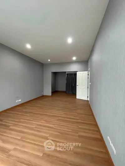 Spacious empty room with wooden flooring and modern lighting, perfect for customization.