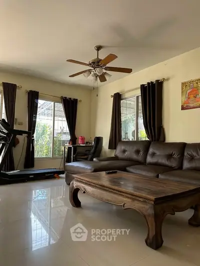 Spacious living room with elegant leather sofa and ceiling fan, featuring a treadmill and large windows.